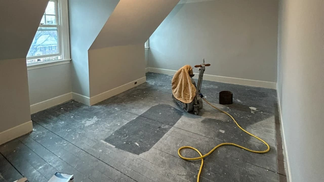 HEPA dust-contained drum sander stripping an old hardwood floor in an attic room