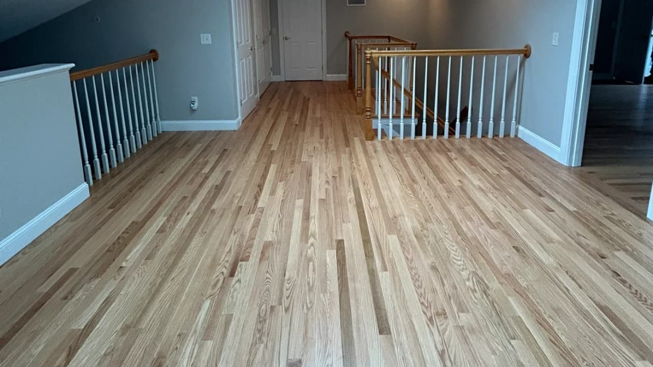Refinished light blonde red oak floor at the top of a staircase landing with white railing