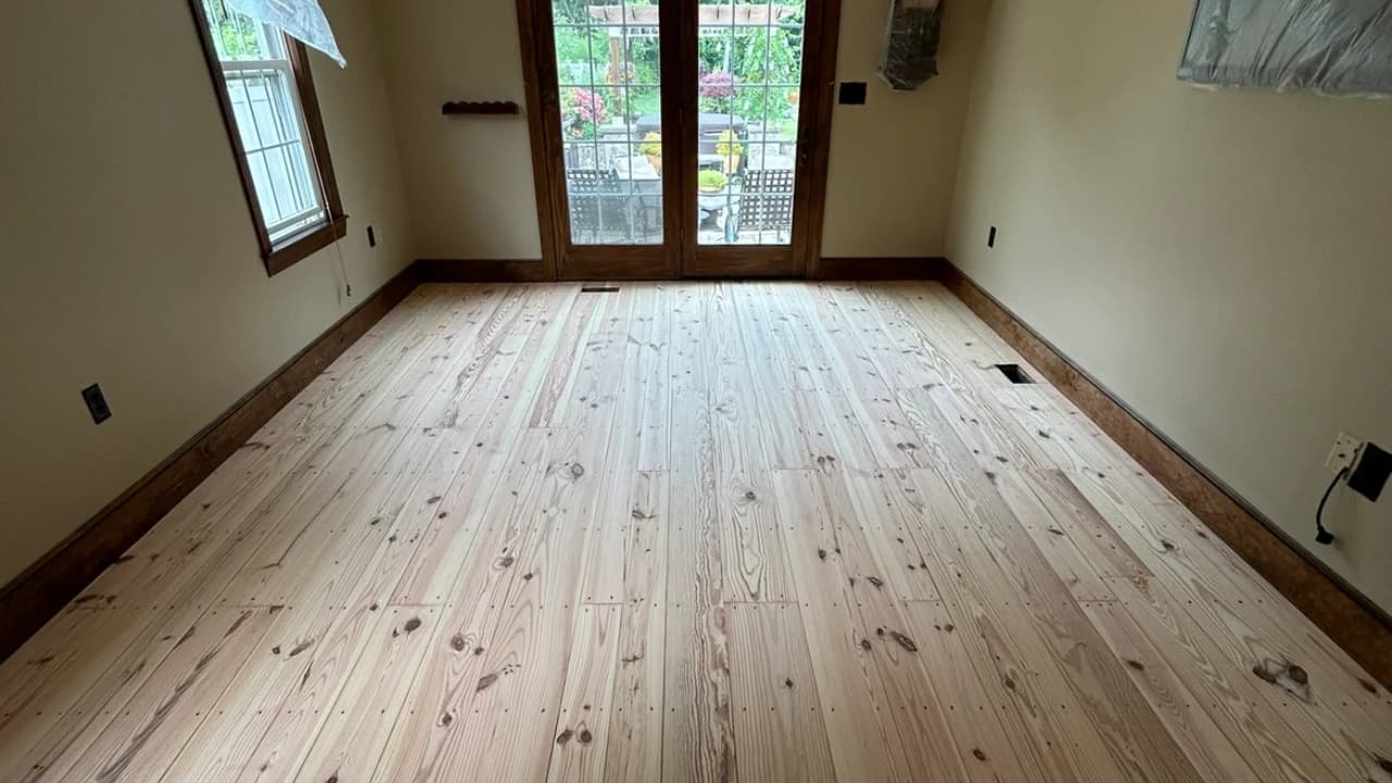 Newly sanded raw pine plank floor before stain in a room with French doors to the garden